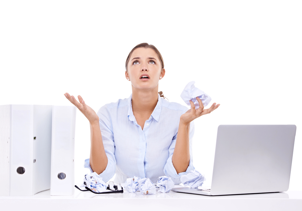 woman sitting at computer throwing hands up in the air with crumpled papers around her.
