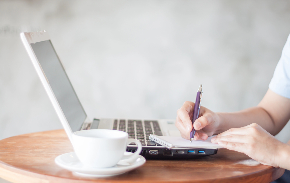 woman sitting at laptop writing notes in notebook