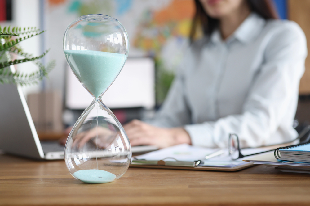 woman sitting at a desk writing content with an hour glass.